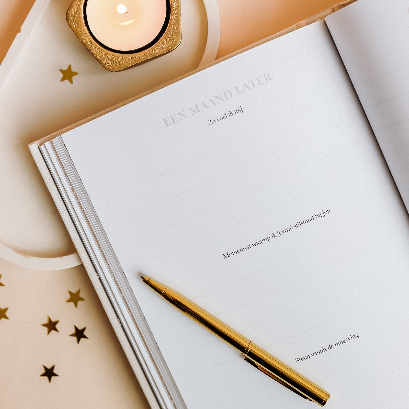 Invulpagina “Een maand later” uit Birth Lines sterrenkindje invulboek met goudkleurige pen, open boek en kaarsje met sterretjes op warme achtergrond
