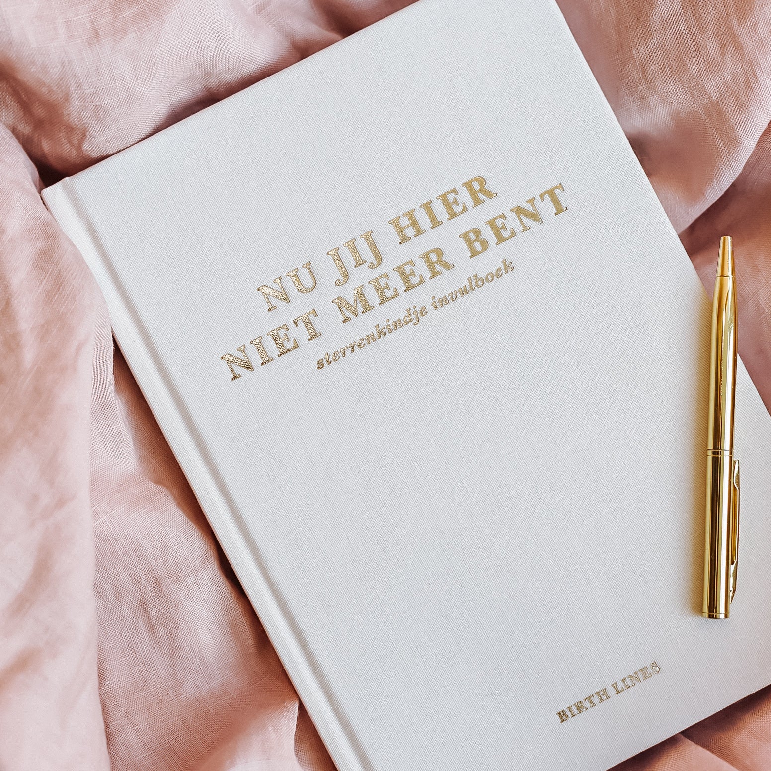 Nu jij hier niet meer bent sterrenkindje invulboek van Birth Lines met linnen kaft en goudfolie titel liggend op zachte roze stof met gouden pen